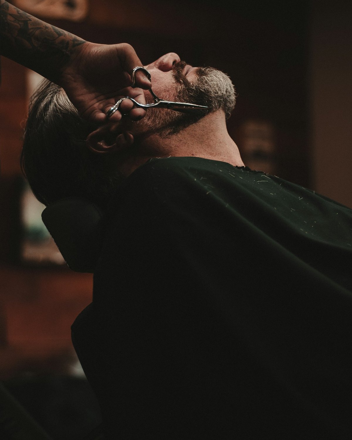 A barber working on a reclined customer, the shop dark behind them